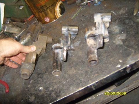 1989 Ford Bronco - Several metal components are laid out on a cluttered workbench, with a hand holding one of them.