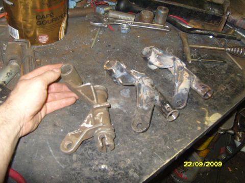 1989 Ford Bronco - Several metal brackets are laid out on a workbench, with a hand holding one of them for examination.