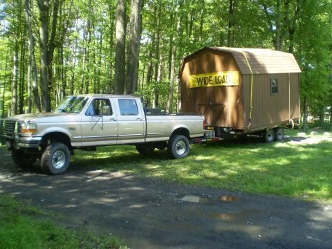 1979 Ford Bronco - A gold Ford F-250 Super Duty tows a shed on a trailer through a wooded area.