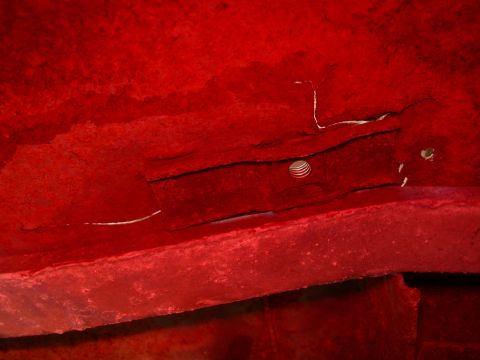 1984 Ford Bronco - Close-up of a red painted vehicle underside showing structural components and a hole with a striped object.