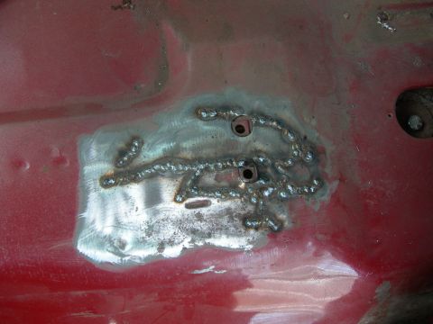 1984 Ford Bronco - Close-up of a welded metal patch on a red vehicle's body, showing repair work.