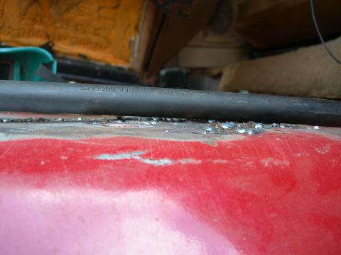 1984 Ford Bronco - Close-up of a red interior surface with a black hose overhead that includes a safety warning.