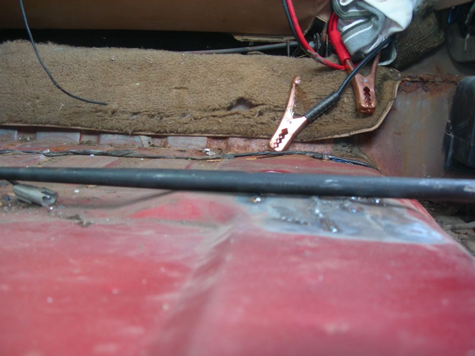 Close-up of vehicle interior floor with jumper cables attached to a battery