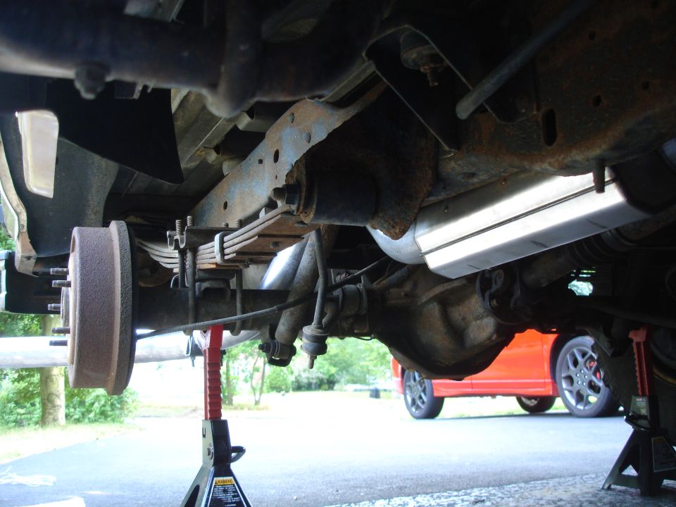 Undercarriage view of rear axle, leaf springs, brake drum and muffler on vehicle supported by jack stands