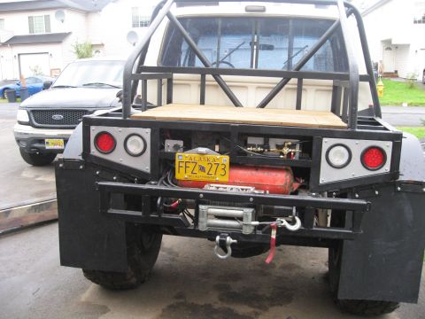 1990 Ford F-250 - This custom truck bed features a winch, auxiliary fuel tank, and a prominent roll cage, with another truck visible in the background.