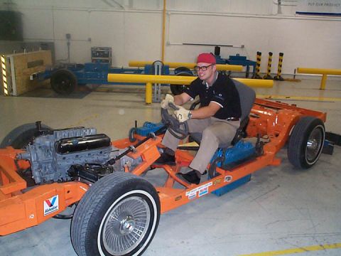 1971 Ford Ranchero - A person sits in the driver's seat of an orange vehicle chassis, with the engine visible.