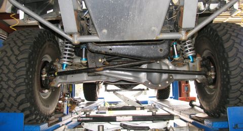 1984 Ford Bronco - The underside of a heavily modified off-road vehicle, showing its robust suspension and drivetrain components.