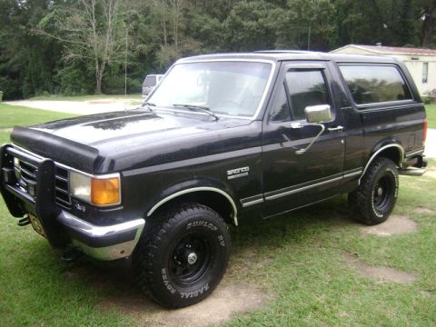 1990 Ford Bronco - A black 1990 Ford Bronco is shown from a three-quarter front angle, parked outdoors on a grassy area.