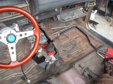 1970 Ford Torino - The interior of a car shows a wooden steering wheel and the exposed floorboards, suggesting a restoration project is underway.