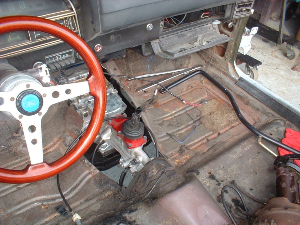Interior of a car with a wooden steering wheel and exposed floorboards