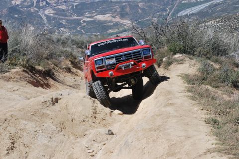 1996 Ford Bronco - Red Ford Bronco tackling a challenging off-road trail with steep inclines and rough terrain.