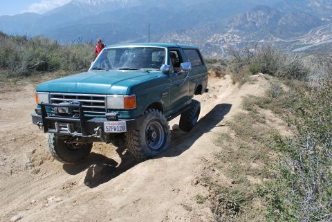 1996 Ford Bronco - This lifted green Ford Bronco navigates a steep dirt trail in a mountainous, arid landscape.