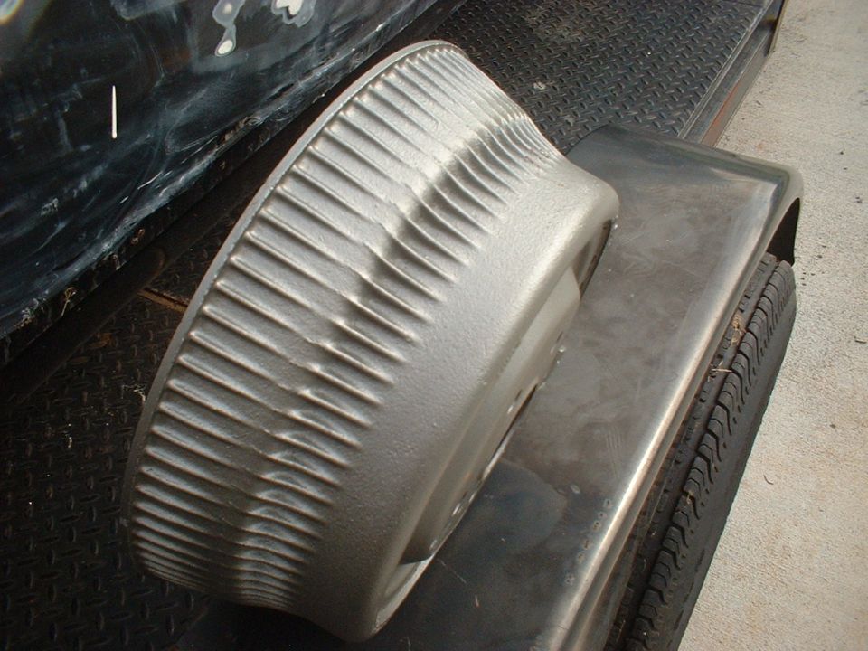 Silver finned brake drum part sitting on metal surface near a tire