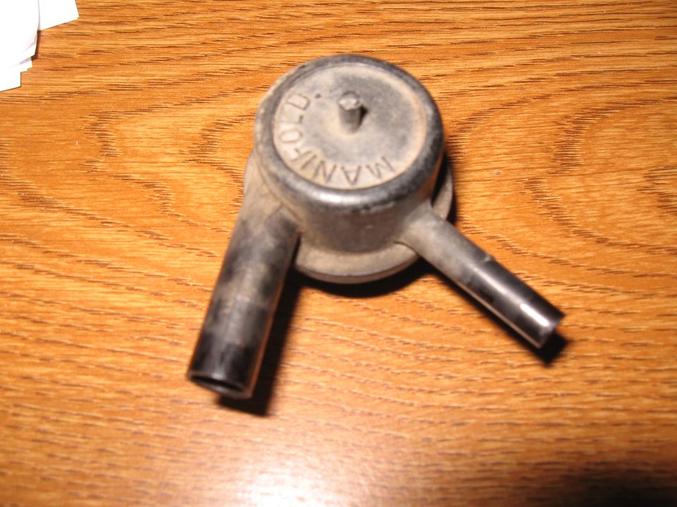 Vacuum advance canister with 'MANIFOLD' visible on top, resting on a wooden surface