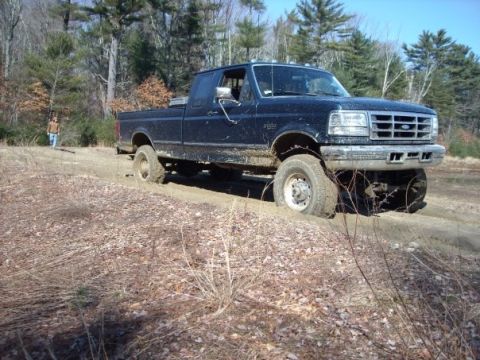 1989 Ford F-150 - A dark blue Ford F-Series truck is stuck in the mud, viewed from the front three-quarter angle. The grille design indicates a 1992-1997 mod…
