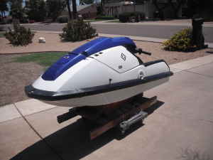1996 Ford Bronco - Blue and white stand-up personal watercraft resting on a wheeled wooden dolly on a residential driveway. The jet ski is shown from a rear t…