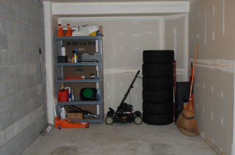 2002 BMW M3 - A collection of items including a lawnmower, tires, and cleaning tools are stored in a garage.