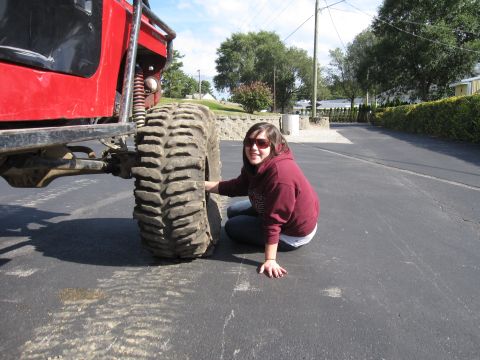 1992 Ford Bronco - A person crouches on pavement beside the front tire of a red lifted 4x4 to show its scale, the tall, aggressive mud-terrain tire stands nea…