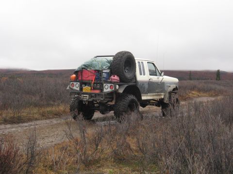 1990 Ford F-250 - Modified Ford F-250 flatbed truck navigates a muddy track through a barren landscape under an overcast sky.