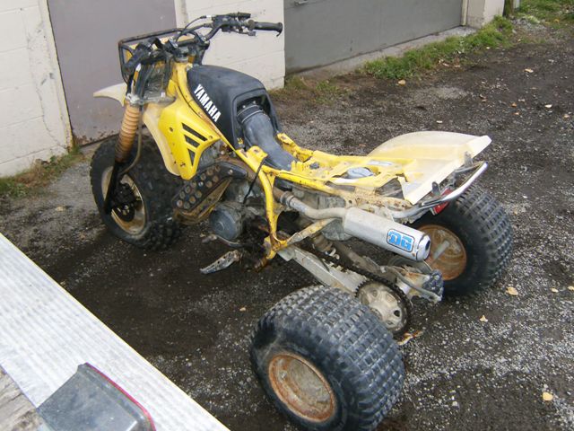 Yellow Yamaha three-wheeled ATV with missing body panels and a damaged rear fender