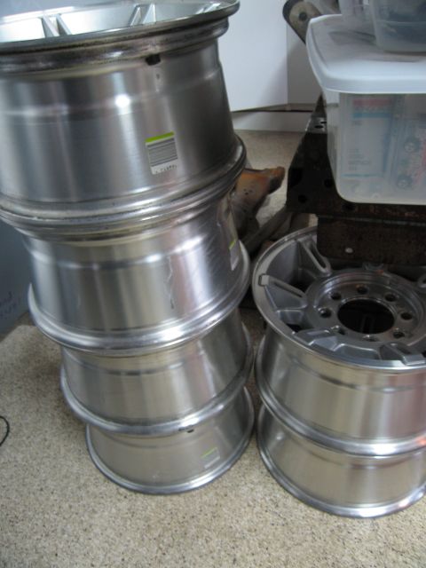 1986 Ford Bronco - Four aluminum wheels are stacked on the left, with a fifth wheel on top. A second stack of two wheels is visible to the right.