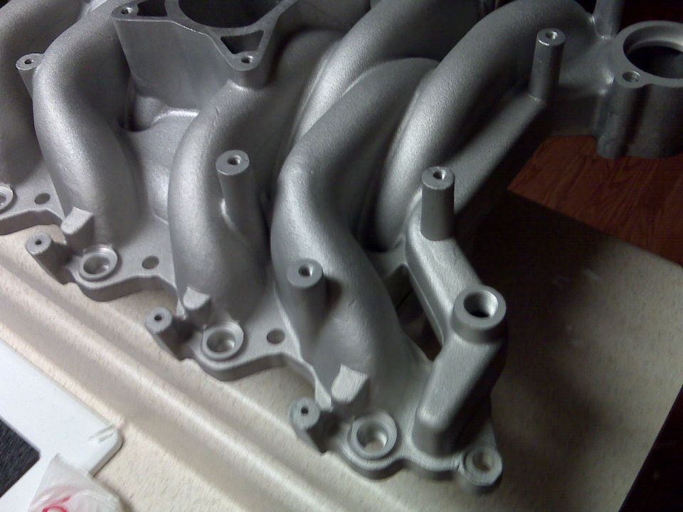 Close-up of a silver aluminum intake manifold with multiple runners and mounting holes
