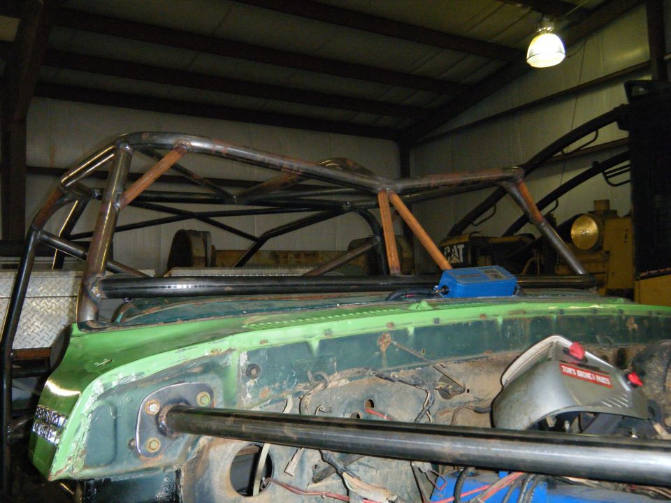 Green vehicle with custom roll cage, front view, showing engine bay and metal fabrication