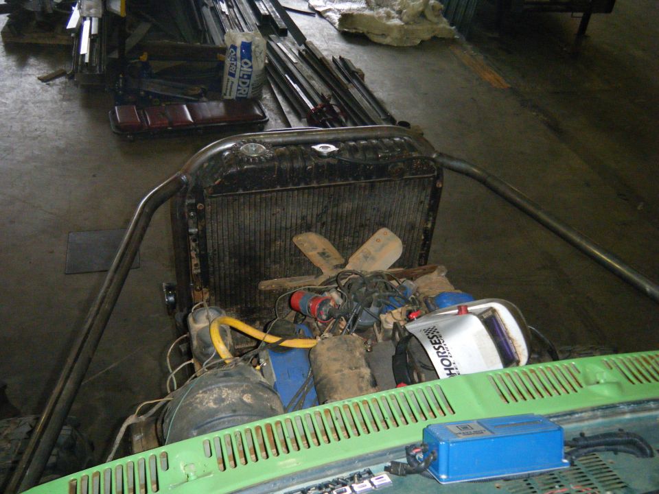 Engine bay with radiator, fan, and various engine components visible. Roll cage tubing is present