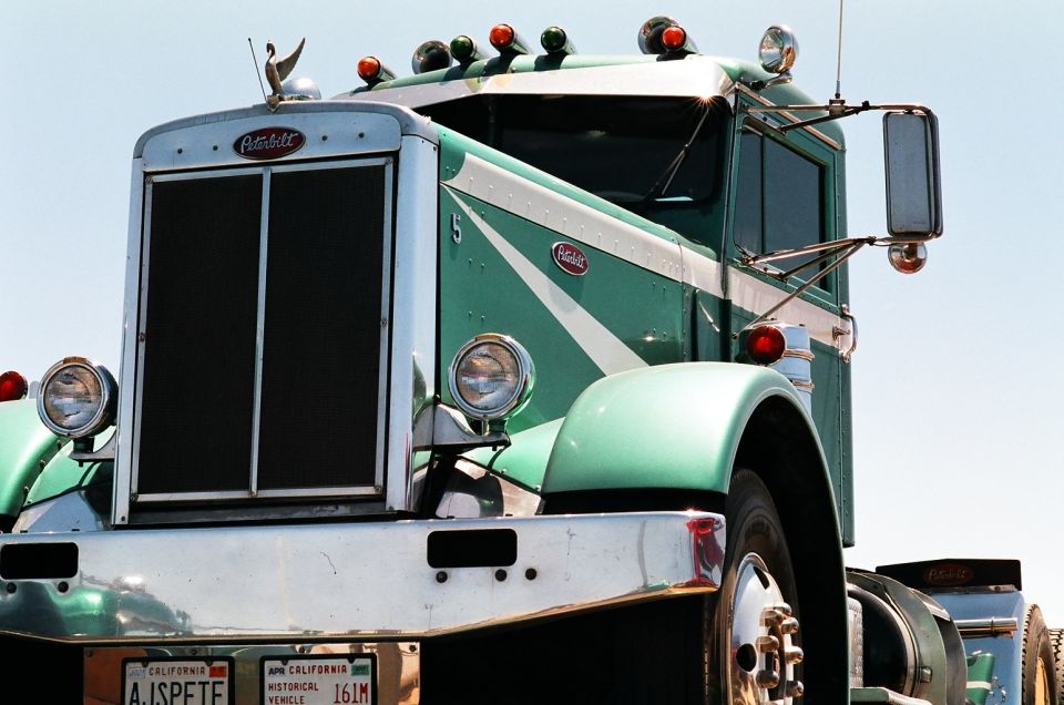 Green Peterbilt truck with chrome grille and bumper, white stripe detail, and California historical vehicle plates