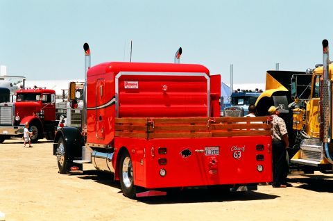 1981 Kenworth W900A - A red flatbed truck with a wooden bed is parked at a show, with other trucks visible in the background.