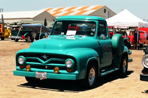 1981 Kenworth W900A - A turquoise 1955 Ford F-100 pickup truck is parked outdoors with other vehicles and buildings in the background.