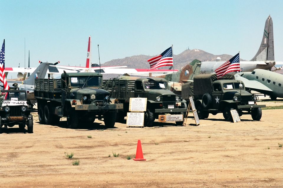 Jeep, two military trucks, and aircraft on display under a clear sky