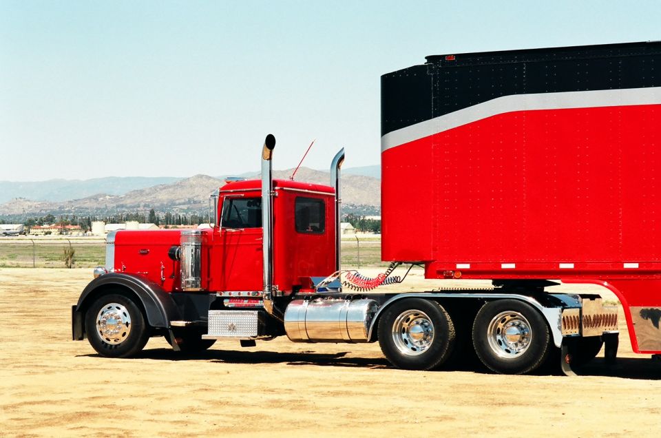Red 1981 Kenworth W900A semi-truck with a black and red trailer, viewed from the front-right