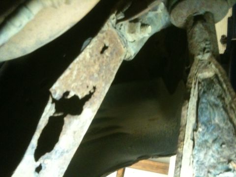 1993 Ford Bronco - The underside of a vehicle shows significant rust and deterioration on its frame components.