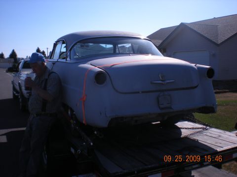 1974 Ford Ranchero - A man stands next to a car being transported on a trailer, with a house in the background.
