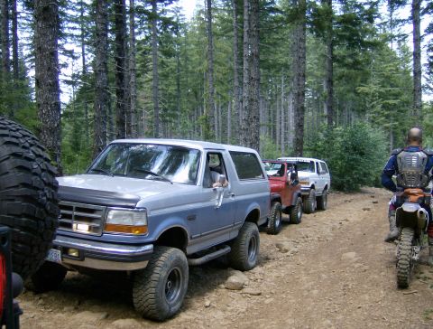 1996 Ford Bronco - A line of off-road vehicles, including a 1996 Ford Bronco, navigates a wooded trail.