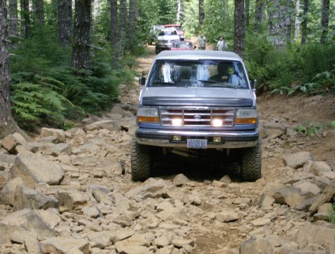 1996 Ford Bronco - Four-wheel drive Bronco navigates a challenging rocky path through a forest.