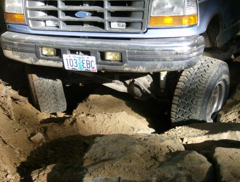 1996 Ford Bronco - This Ford truck is navigating a rocky and uneven terrain, with its front tires positioned on large rocks.