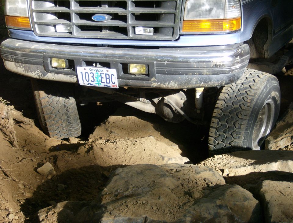 Front of a blue Ford truck with its tires on rocks and dirt