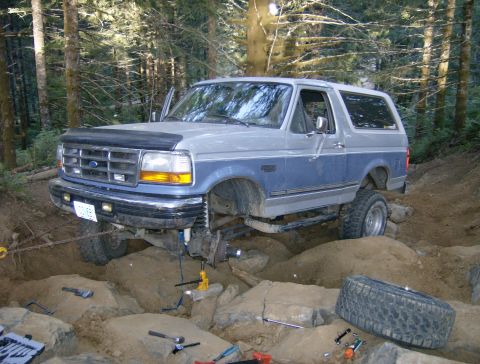 1996 Ford Bronco - A two-tone blue and gray Ford Bronco is shown off-roading with its suspension lifted high over rocks.