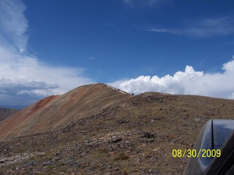 1994 Ford Bronco - Several off-road vehicles traverse a rocky mountain ridge on a clear day with dramatic clouds overhead.