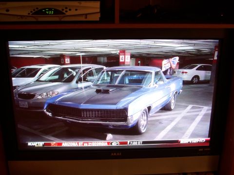 1971 Ford Ranchero - A blue pickup truck with a black hood and scoops is parked in a garage next to other vehicles.