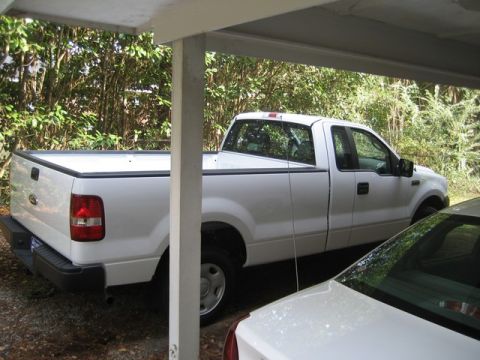 2004 Ford F-150 - This white 2004 Ford F-150 pickup truck is seen parked under a carport, partially obscured by another vehicle.