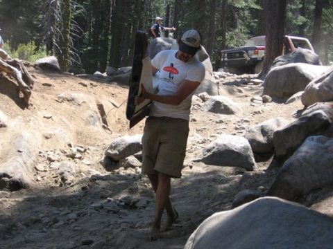1991 Ford Bronco - A man carries a car door through a rocky off-road area, with another vehicle visible in the distance.