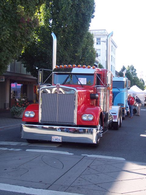 1981 Kenworth W900A - A red 1981 Kenworth W900A semi-truck is parked in a line with other vehicles on a street.