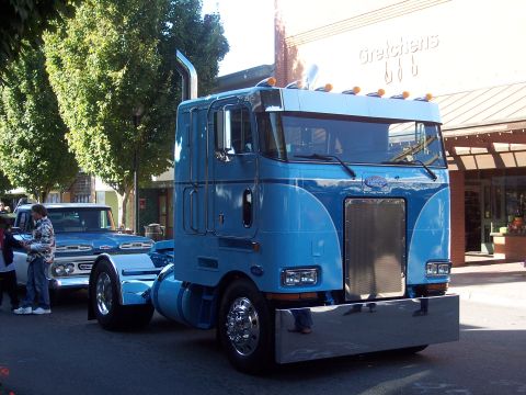 1981 Kenworth W900A - A bright blue semi-truck is parked on a street, with another older model truck behind it.
