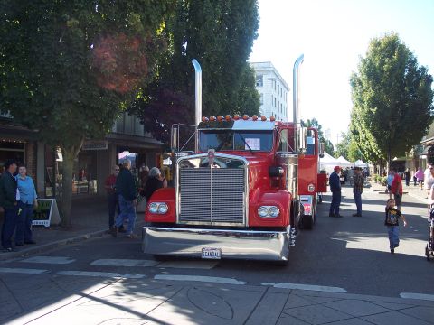 1981 Kenworth W900A - A bright red semi-truck is parked on a street, with people milling about in the background.