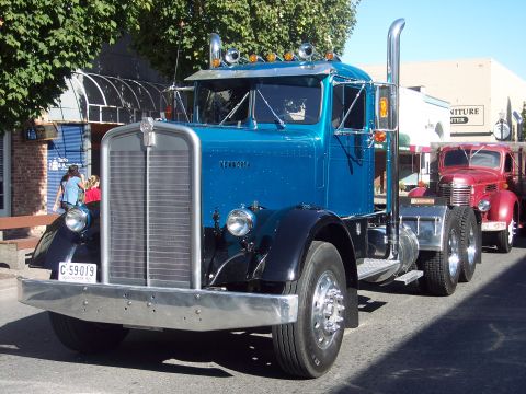 1981 Kenworth W900A - A blue 1981 Kenworth W900A semi-truck is parked on a street, with another vintage truck visible behind it.