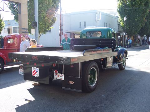 1981 Kenworth W900A - A vintage GMC flatbed truck is parked on a street, with another truck visible to its left.