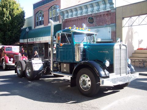 1981 Kenworth W900A - A teal Kenworth truck is parked on a street in front of a store, with another vintage truck to its left.